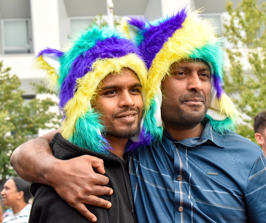 Two men wearing colorful furry hats, standing closely together in a festive atmosphere.