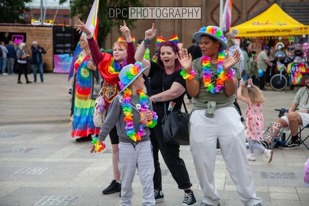 A lively group of people celebrating at a festival, some wearing colorful outfits and flower leis, with children participating in the festive atmosphere.