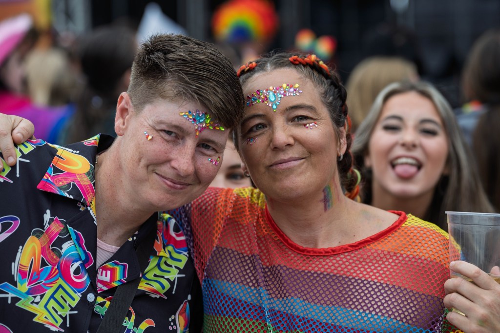 Two individuals posing together at a lively event, both adorned with colorful outfits and face decorations, embodying a festive atmosphere.
