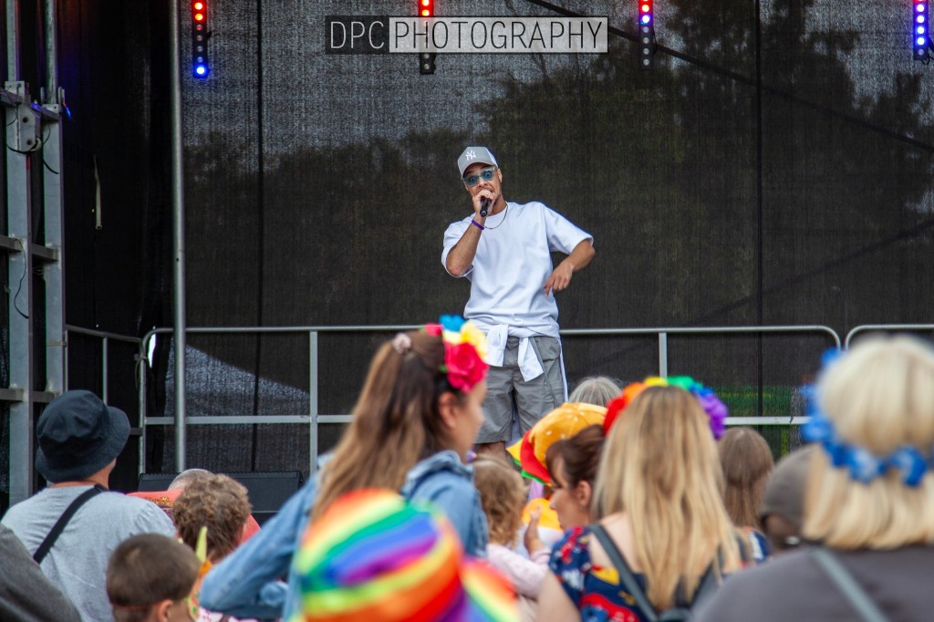 A performer singing into a microphone on stage, surrounded by an engaged audience wearing colorful accessories.