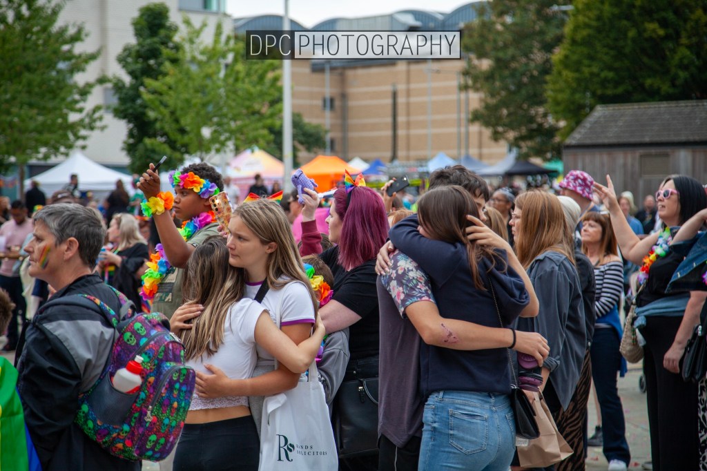 A diverse crowd of people celebrating together at a festive event, wearing colorful accessories and embracing each other.