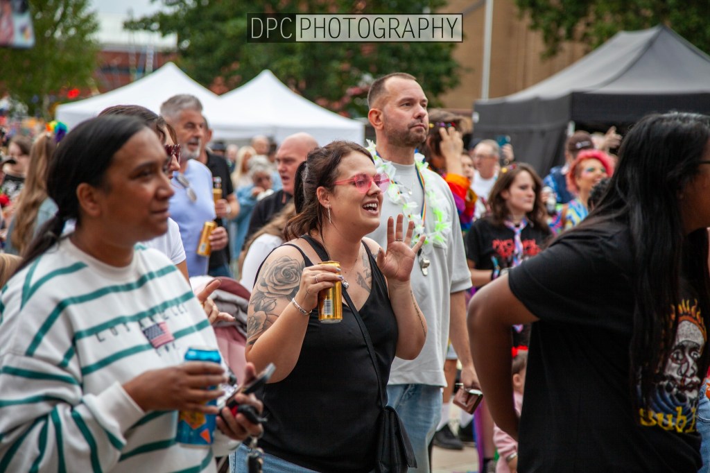A lively crowd at an outdoor event with people enjoying the atmosphere, some holding drinks and engaging with the performance.