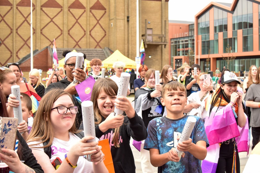 A crowd of young people smiling and holding colorful rolls and bags, celebrating an event outdoors.