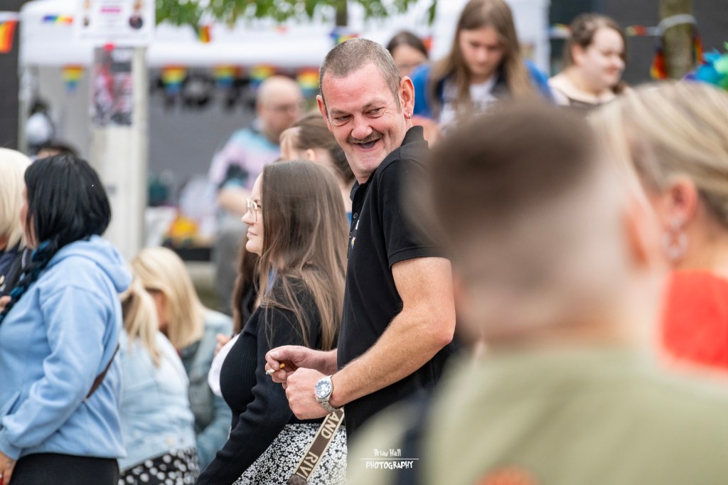 A man smiling and enjoying a lively outdoor event, surrounded by a diverse crowd of people.