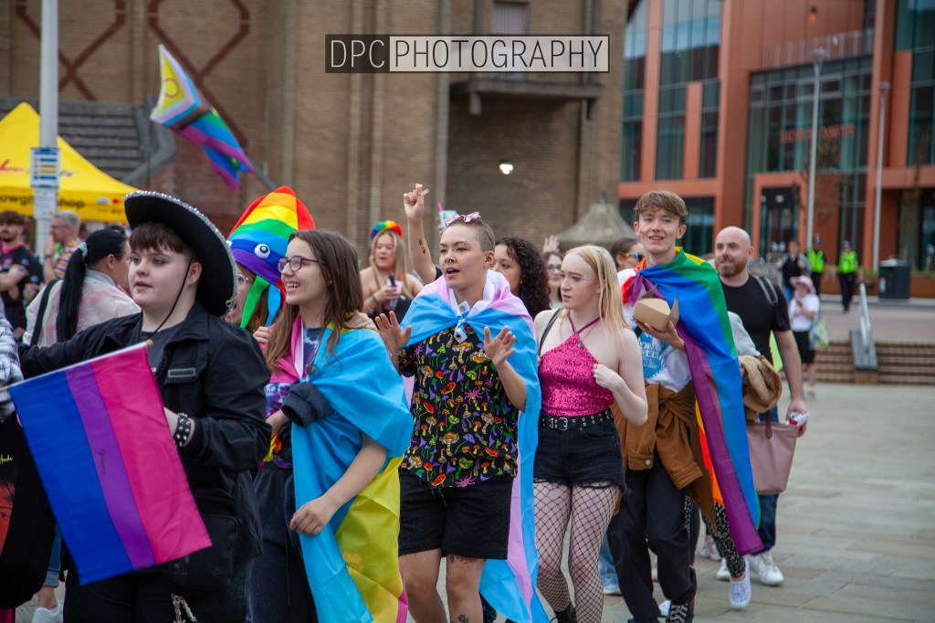 A group of diverse individuals celebrating at a pride event, wearing rainbow flags and colorful outfits, showing solidarity and joy.