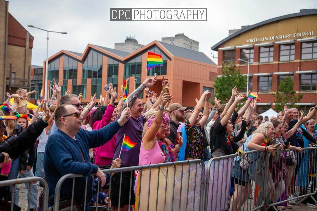 A vibrant crowd at a pride event, celebrating with flags and cheering. People are showing their support and joy, wearing colorful outfits and accessories.